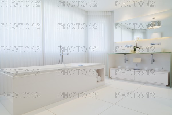 White elongated rectangular bathtub and cabinets with large wall mirror in en suite with ceramic