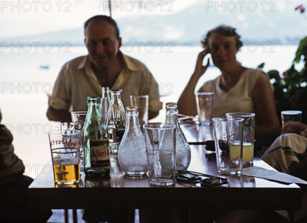 Menschen um einen Tisch mit Getränken und Flaschen in einem Hafencafé in Calvi, Korsika,