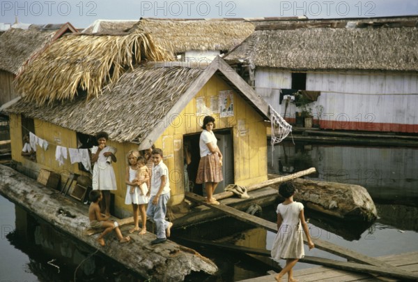 Woman and children in an informal housing area with wooden huts built on logs, known as the