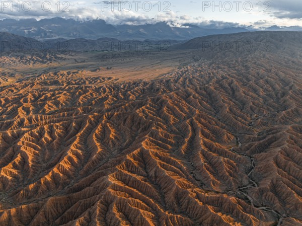 Landscape of eroded hills, badlands at sunset, mountain peaks of the Tian Shan Mountains in the