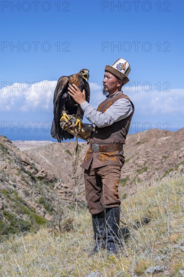 Traditional Kyrgyz eagle hunter with eagle in the mountains, near Kysyl-Suu, Kyrgyzstan, Asia