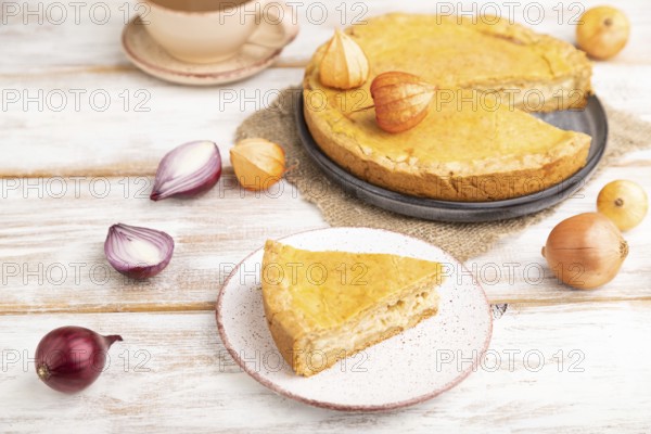 Autumn onion pie and cup of coffee on white wooden background and linen textile. Side view, close