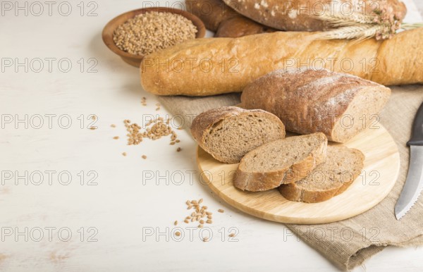 Sliced bread with different kinds of fresh baked bread on a white wooden background. side view,