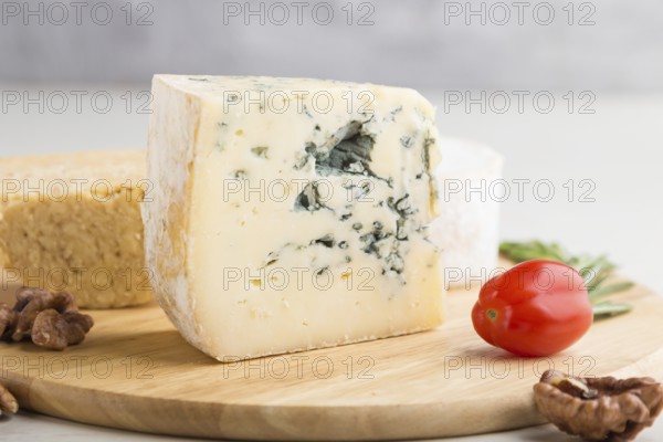 Blue cheese and various types of cheese with rosemary and tomatoes on wooden board on a white