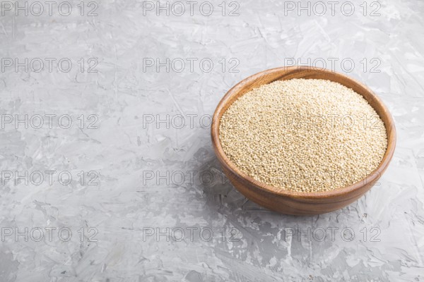 Wooden bowl with raw white quinoa seeds on a gray concrete background. Side view, close up, copy