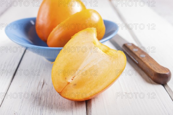 Ripe orange persimmon in a blue plate on white wooden background, with copy space