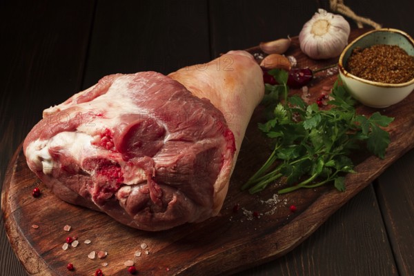 Raw pork knuckle, on a wooden chopping board, with spices, close-up, top view, no people