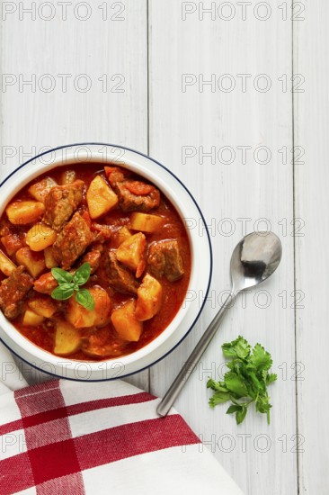 Potatoes stewed with meat, in tomato sauce, with spices and herbs, no people, on a white table