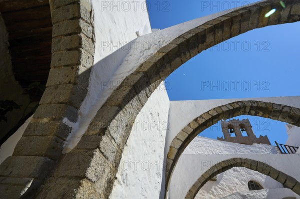Stone arch and bell tower on a sunny day, Part of a medieval monastery with white walls, Inside the