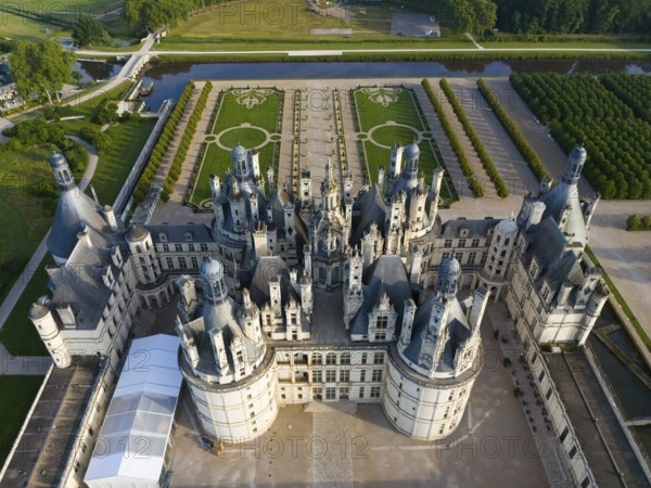 Detailed view of a historic castle from the air, with many towers and green areas all around,
