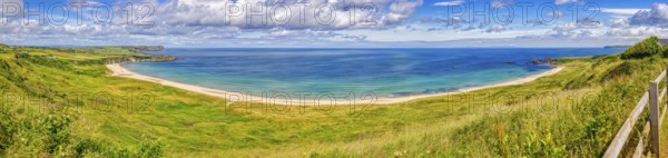 Wide beach with green meadow and wide sea under a blue, cloudy sky, County Antrim Coast