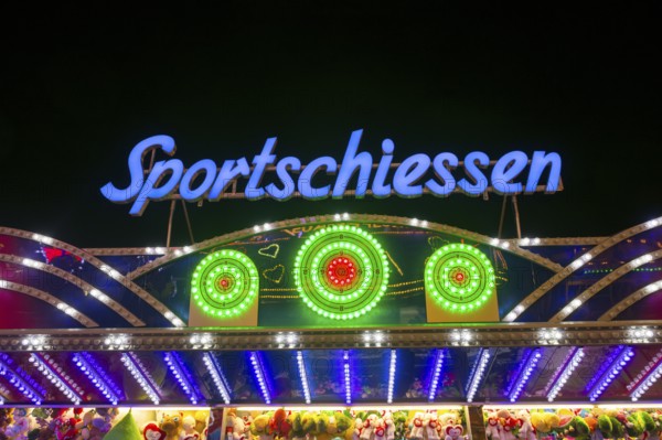 Illuminated sports shooting sign on a fairground stand with colourful lights at night, Cannstatter