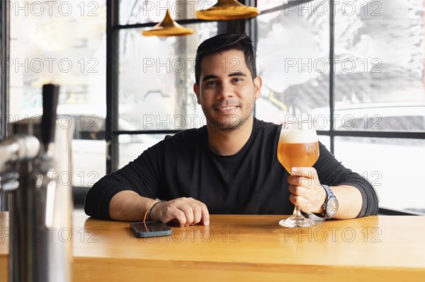 A young Latin man enjoys a refreshing lager beer in a chic, modern bar. He is sitting at the