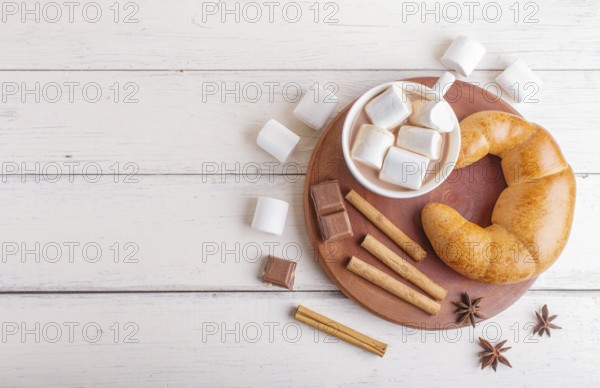 A cup of hot chocolate with marshmallow, croissant and spices on white wooden background. top view,
