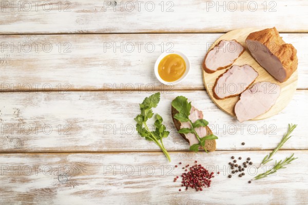 Smoked pork ham on cutting board with pepper and herbs on white wooden background. Top view, flat