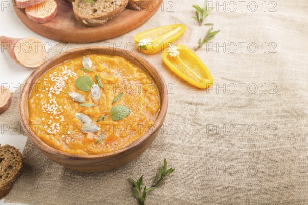 Sweet potato or batata cream soup with sesame seeds in a wooden bowl on a white wooden background