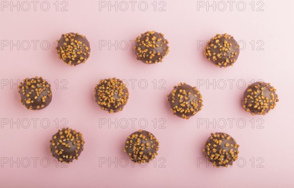 Chocolate caramel ball candies with almonds in a row on a pastel pink background. top view, flat