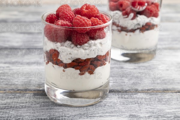 Yogurt with raspberry, goji berries and chia seeds in glass on gray wooden background. Side view,