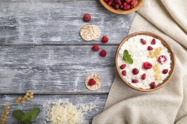 Rice flakes porridge with milk and strawberry in wooden bowl on gray wooden background and linen