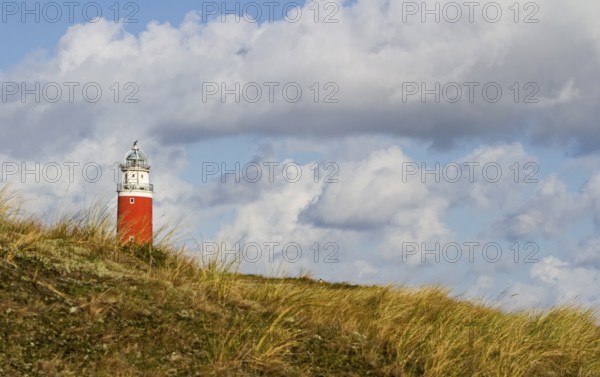 A red lighthouse stands on a grassy hill under a dramatic cloudy sky, Eierland lighthouse, Texel