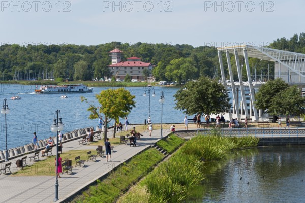 A lively lakeside promenade with a view of the lake, boats and an architectural bridge in the
