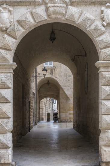 Narrow corridor with arches and stone walls, illuminated by ancient lanterns in a historic