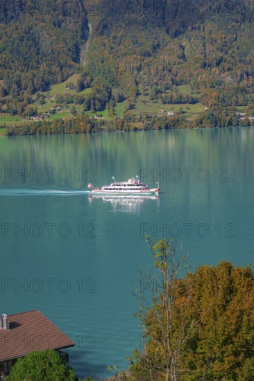 A ship cruises across the lake, against a background of forested mountains in autumn colours, Lake
