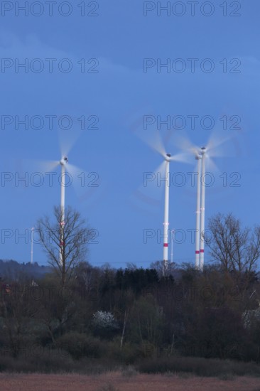 Luminous wind turbines rotating in an area surrounded by trees in the evening light, Wind turbines