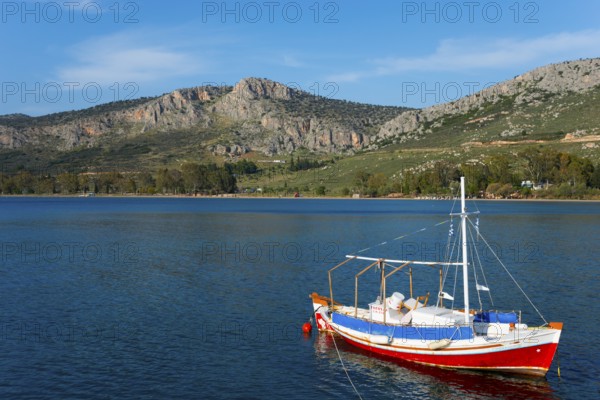 Small boat on a calm sea with mountains and blue sky in the background, Agia Kyriaki, Nafplio,