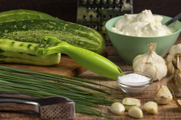 Fresh ingredients such as cucumbers, garlic, chives and sour cream on a wooden table with a peeler