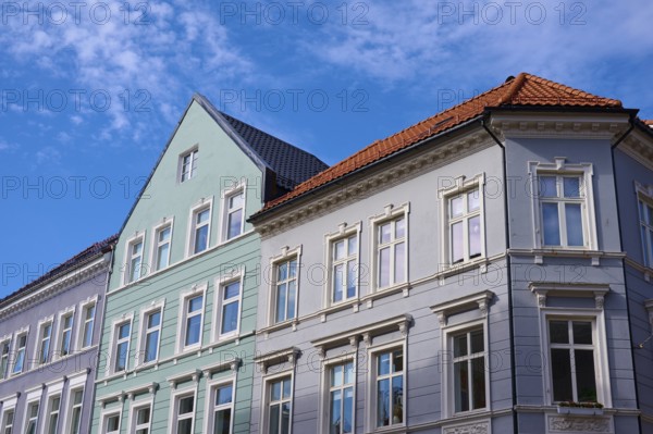 Several old buildings with different facade colours and red roof tiles in front of a blue sky with