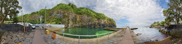 360° view, wooden walkway leading to green rocky coast and clear ocean under blue sky with clouds,