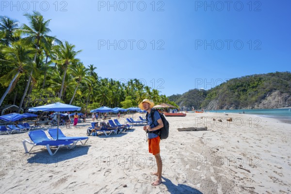 Tourist on a sandy beach with deckchairs, tropical island with palm trees and turquoise blue sea,