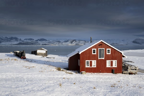 Historic mine railway and red house in front of the wintry, snow-covered Kongsfjorden, Ny-Ålesund,