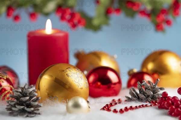 Red and gold Christmas baubles next to a lit candle on artificial snow, decorative festive