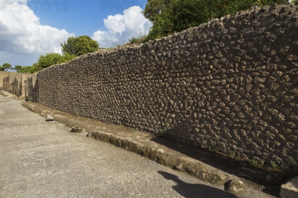 Long compacted crushed stone paved street with sidewalk and old stone walls plus residential