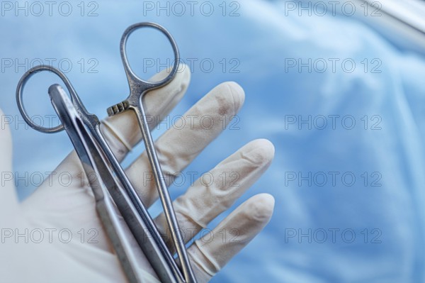 Gloved hand holding forceps with a blue background, indicating surgery preparation