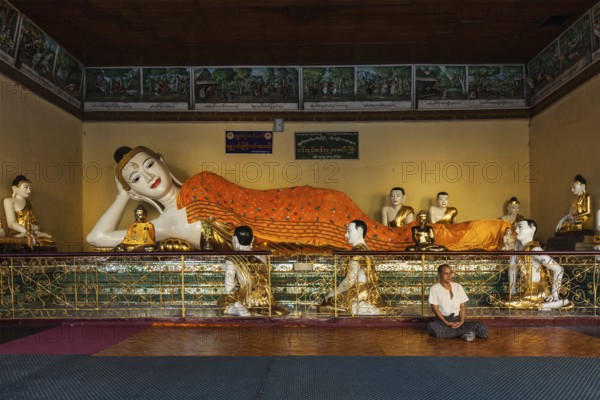YANGON, MYANMAR, JANUARY 3, 2014: Man meditating near statue of Recumbent Buddha in Shwedagon Paya