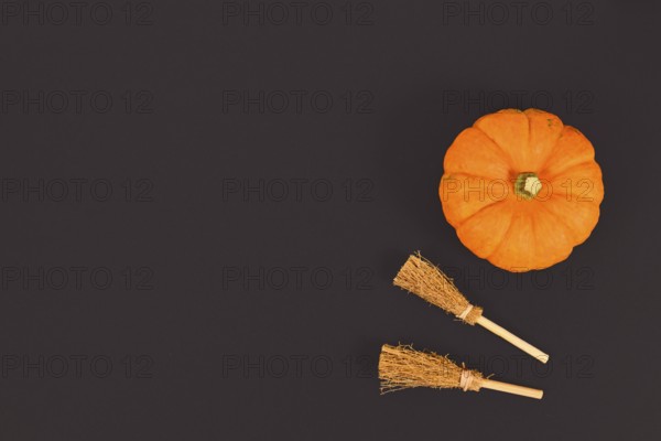 Orange Halloween pumpkin and witch brooms in corner of black background with copy space