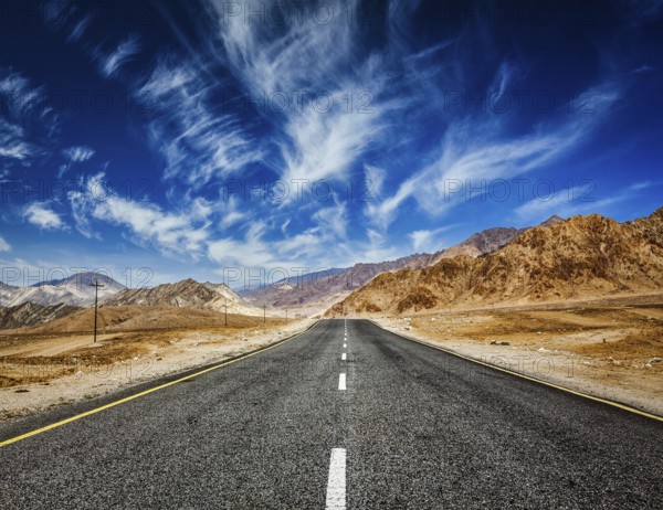 Travel forward concept background, road in mountains Himalayas with dramatic clouds on blue sky.