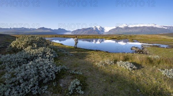 Tourist standing on the lakeshore, reflection in a lake, view of glacier tongues Skaftafellsjökull