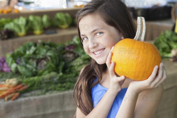 Happy young blue eyed girl holding a fresh pumpkin at the farmers market