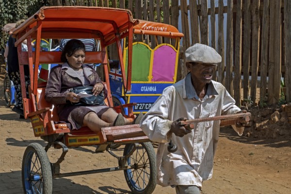 Old Malagasy man pulling pousse-pousse, pulled rickshaw with local woman in the city Antsirabe,