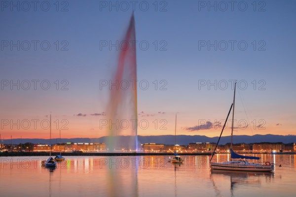 The Jet d'eau at dusk is the landmark in Geneva's harbour basin, with sailboats in the foreground