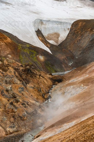 Steaming stream between colourful rhyolite mountains and snowfields, Hveradalir geothermal area,