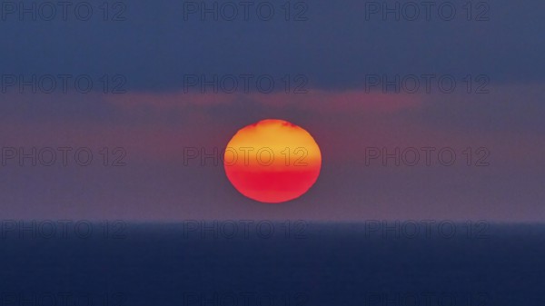 Sun as a fiery red big ball, blue-purple sky, sun just above the horizon, sunset, evening light,