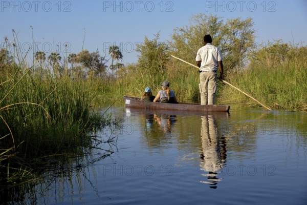 Tourists in a mokoro or dugout boat on safari in swamp area, Gomoti Plains Camp, Gomoti Concession