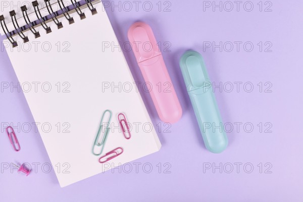 Clipboard with pink and blue text markers and paper clips on purple background with empty copy