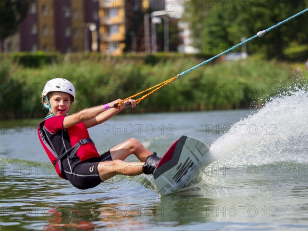 Boy or girl, water sports with wakeboard, red life jacket, water skiing in the wake park