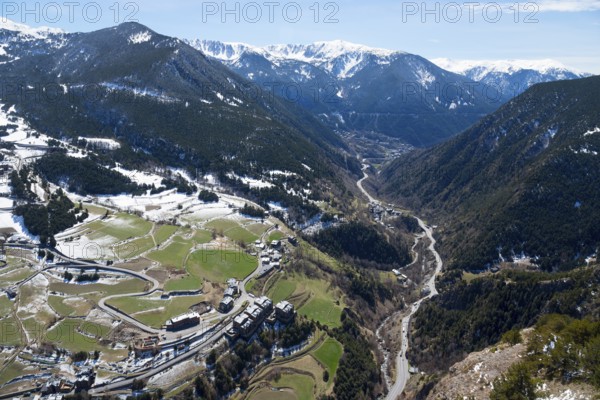 Bergtal mit einem Fluss, grünen und verschneiten Flächen und einer Straße, die sich durch das Tal